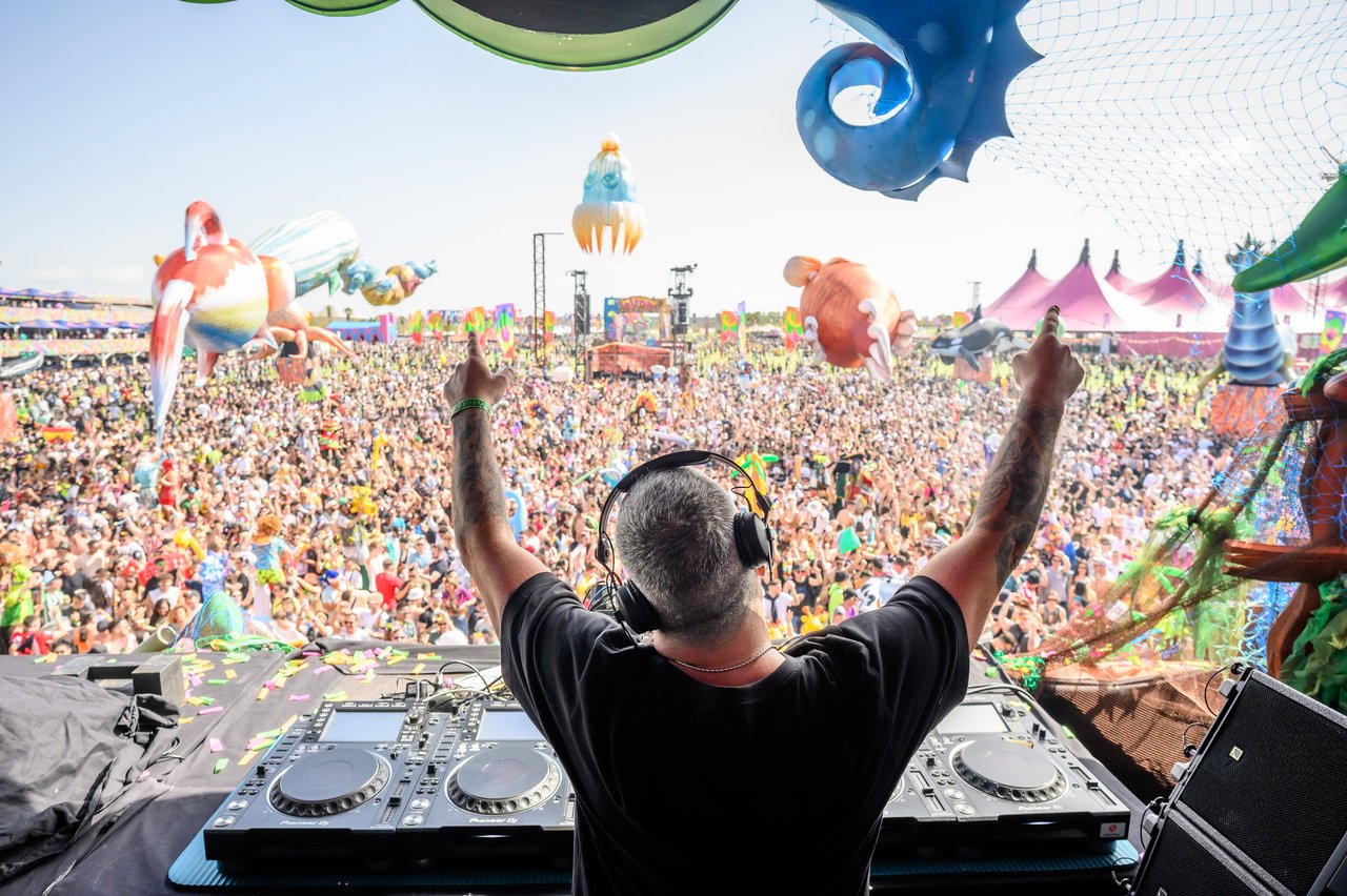 DJ comandando a pista da elrow com os braços erguidos diante da multidão