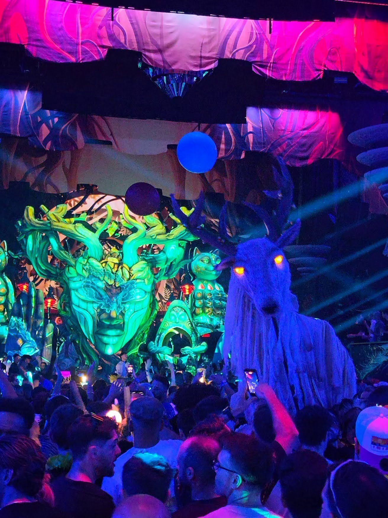 Cenografia da elrow: rosto verde gigante, gato e cervo iluminados sobre a pista