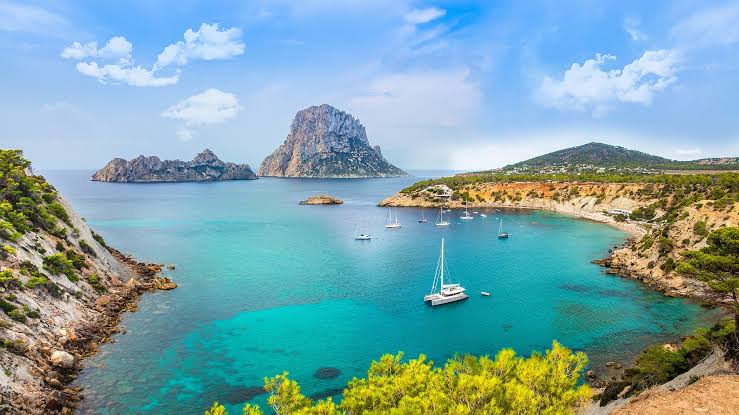Es Vedrà visto da enseada de Cala d'Hort, em Ibiza, com veleiros ancorados na água turquesa