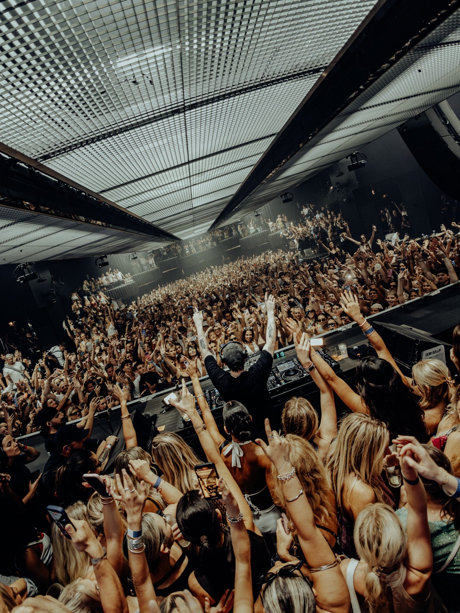 DJ na cabine e pista cheia de gente com as mãos para o alto em clube de Ibiza
