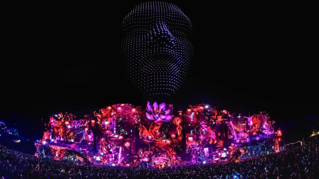 Show de drones formando um rosto sobre o Mainstage iluminado de rosa e vermelho, à noite, no Tomorrowland Brasil.
