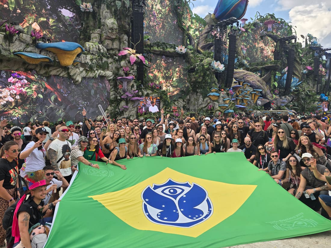Viajantes da Never Ends abrindo a bandeira gigante do Brasil com o símbolo do Tomorrowland Brasil diante do Mainstage LIFE, em 2025.
