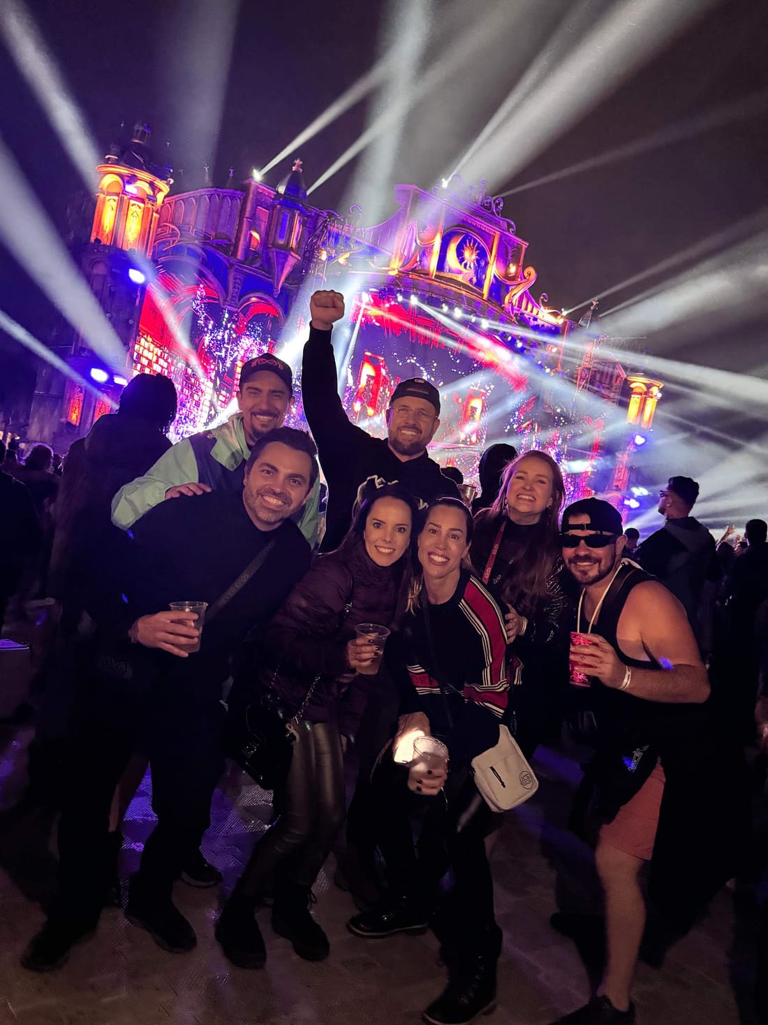 Viajantes da Never Ends comemorando à noite entre os feixes de luz de um palco do Tomorrowland Brasil 2025.