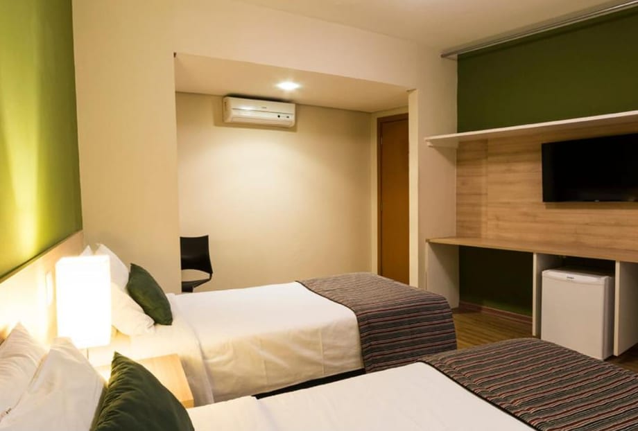 Apartamento duplo solteiro do Hotel Never Ends: duas camas, TV na parede de madeira, frigobar e ar-condicionado.