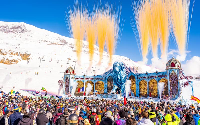O palco do leão do Tomorrowland Winter em plena pista de esqui, com fogos dourados de dia